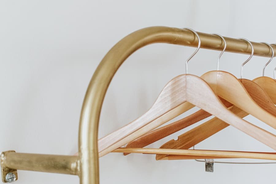 Perchero dorado con perchas de madera vacías contra una pared blanca