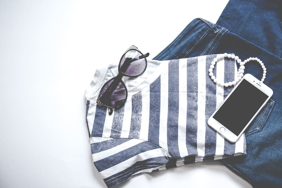 Camiseta de rayas, vaqueros, gafas de sol y pulsera de perlas ordenados sobre un fondo blanco