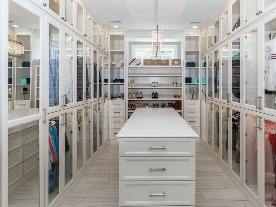 Vestidor blanco con armarios acristalados, isla central y zapatos ordenados en los estantes