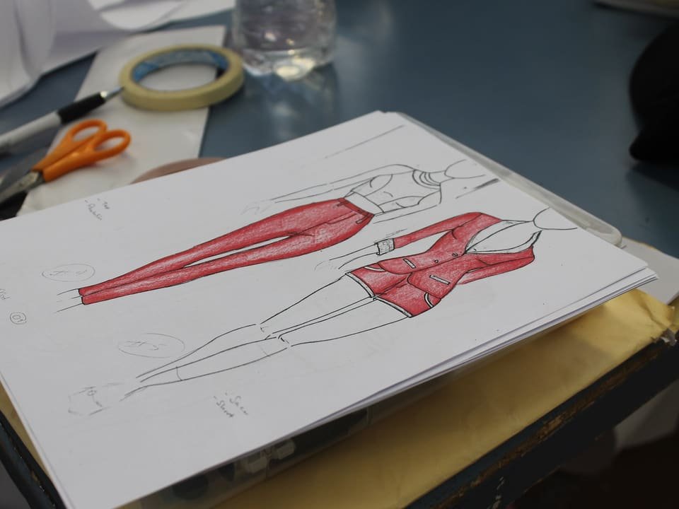 Bocetos de diseño de moda de un conjunto rojo sobre una mesa, junto a tijeras, regla y cinta adhesiva