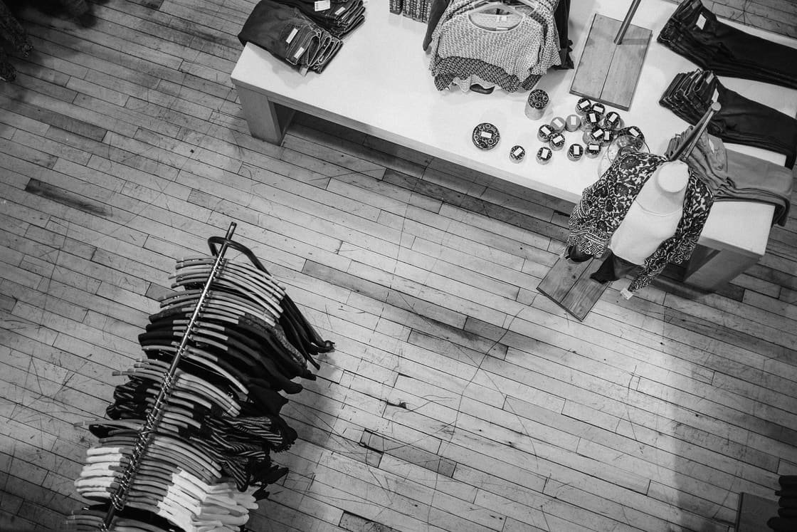 Vista cenital en blanco y negro de una tienda de ropa, con un perchero y una mesa de prendas dobladas