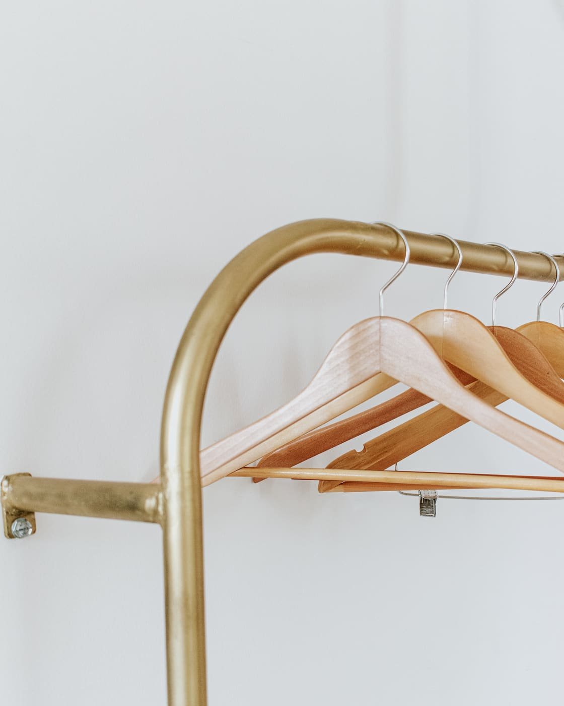 Perchero dorado con perchas de madera vacías contra una pared blanca